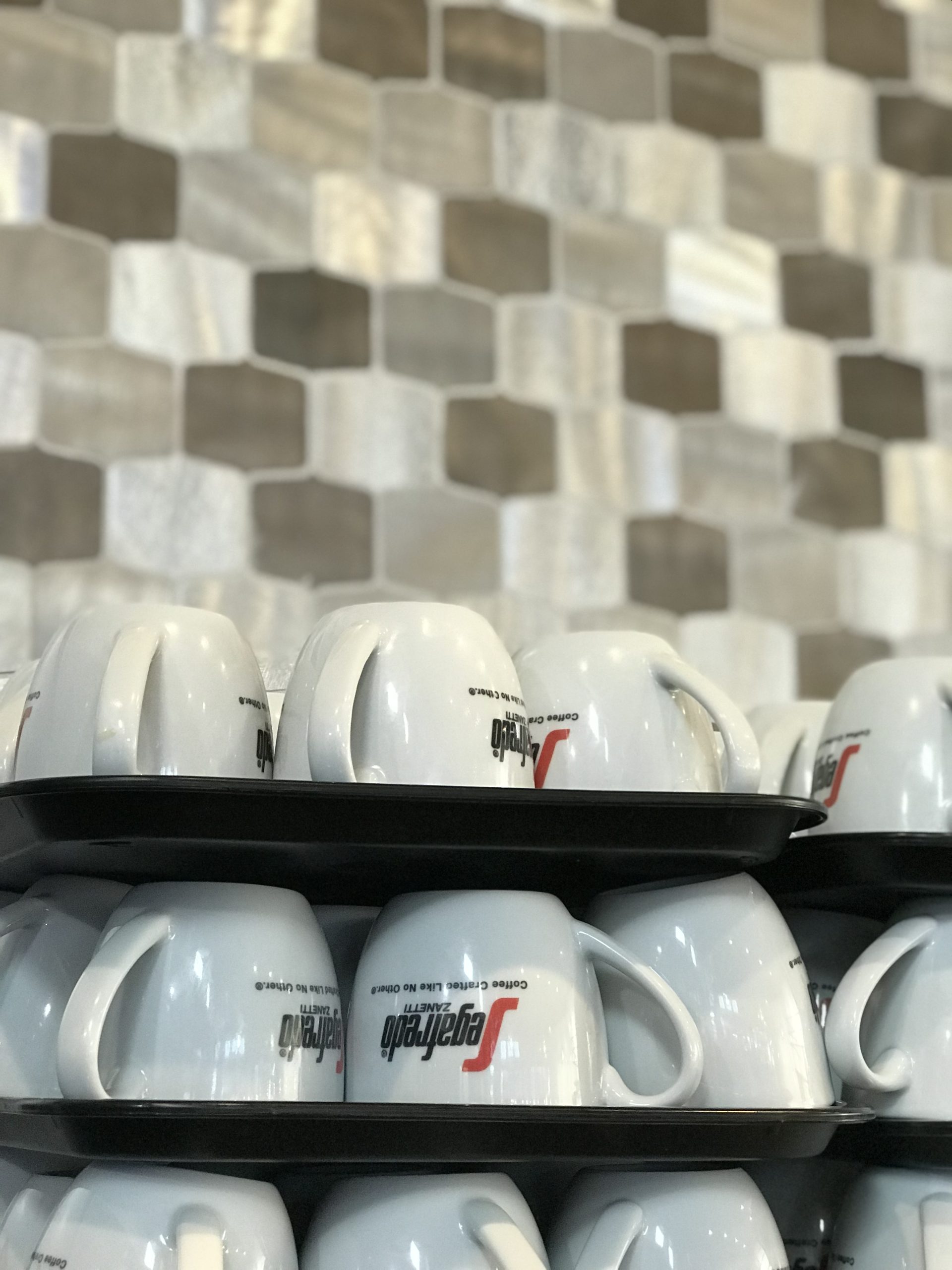 Two trays stacked on top of each other with Segafredo brand coffee mugs on them in front of a decorative background